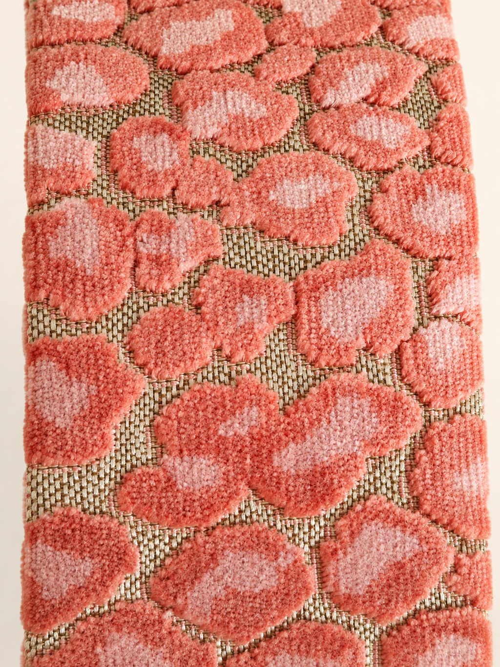 Detail van zalmroze jacquardstof met zacht reliëfpatroon op goudkleurige geweven ondergrond