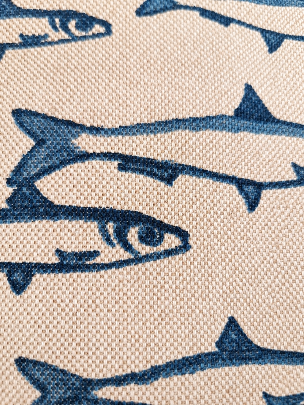 Detail van de geweven naturel stof met blauwe vissenprint.