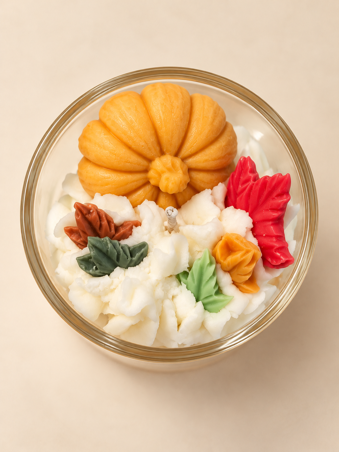 Bovenaanzicht van de Pumpkin Spice geurkaars met een oranje pompoen, herfstblaadjes van was en een witte decoratieve topping.